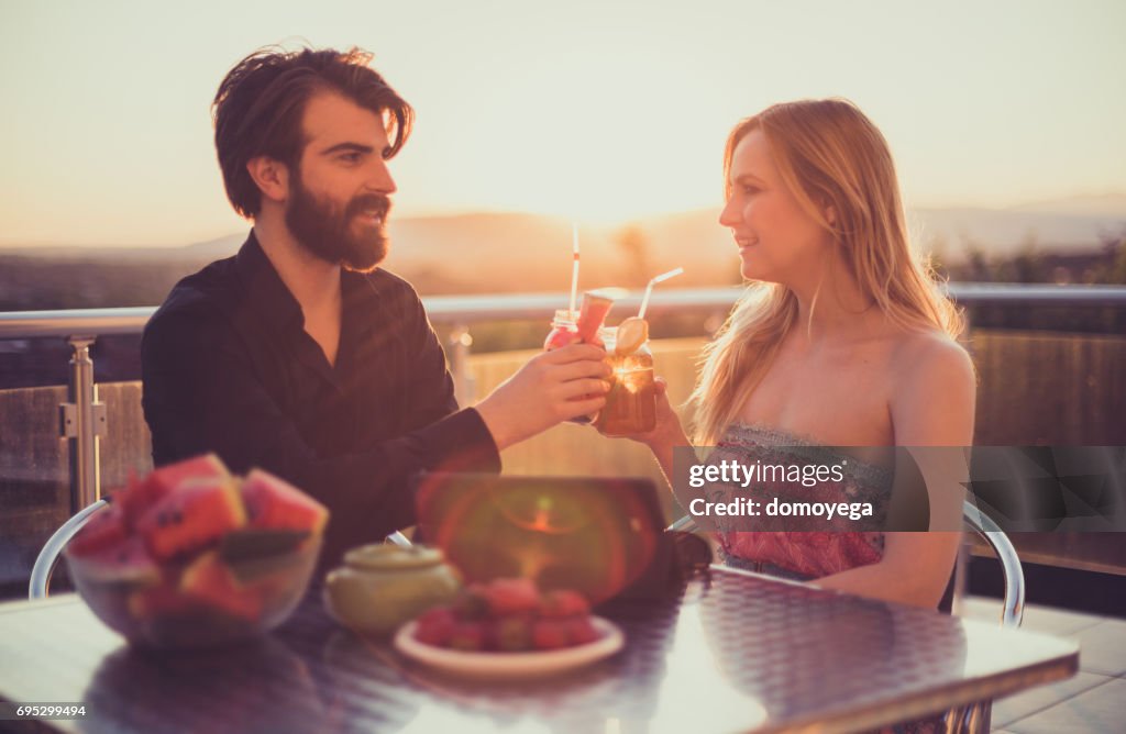 Beautiful young couple eating fruit salad and drinking smoothies on the balcony on a sunny summer day