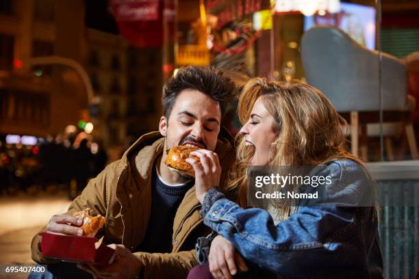 cheerful woman feeding burger to man at night - swallow imagens e fotografias de stock