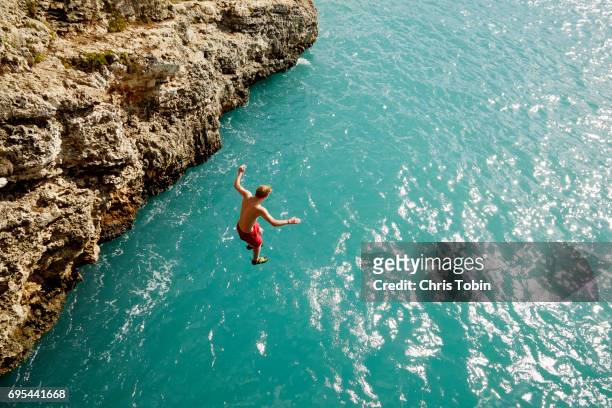 teenager jumping off cliff into shimmering blue water - brant klippa bildbanksfoton och bilder