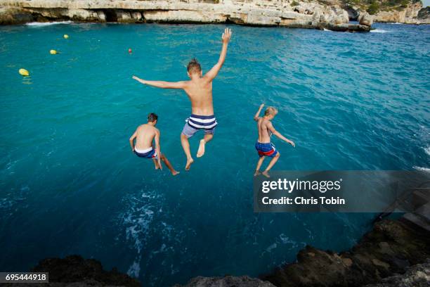 three teenage boys jumping into blue water with arms outstretched - adventure　sea stock-fotos und bilder