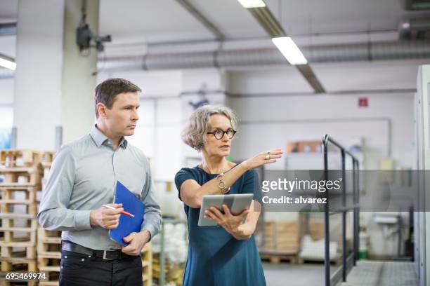 manager che discute con un operaio maschio presso l'impianto di stampa - digital printing foto e immagini stock