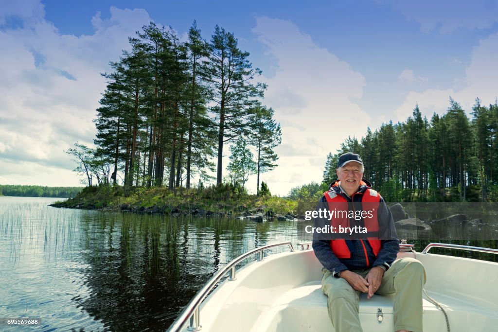 Lächelnd 73 Jahre alt Senior trägt eine Kappe und eine Schwimmweste sitzt vor einem Motorboot Segeln in Gastrikland, Schweden