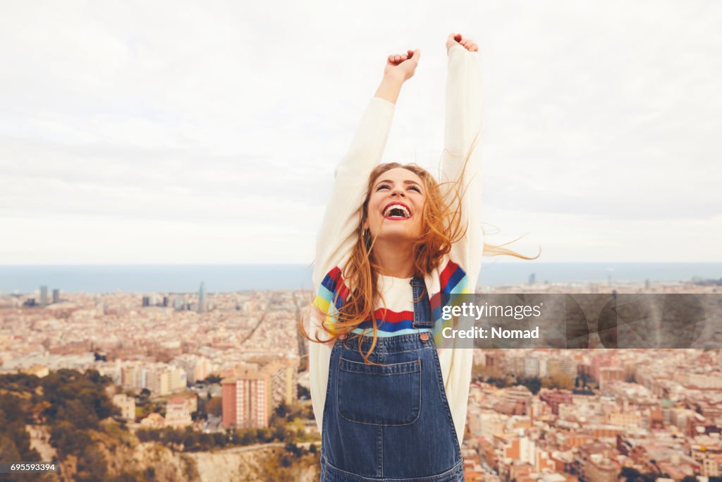 Happy woman with arms raised against cityscape