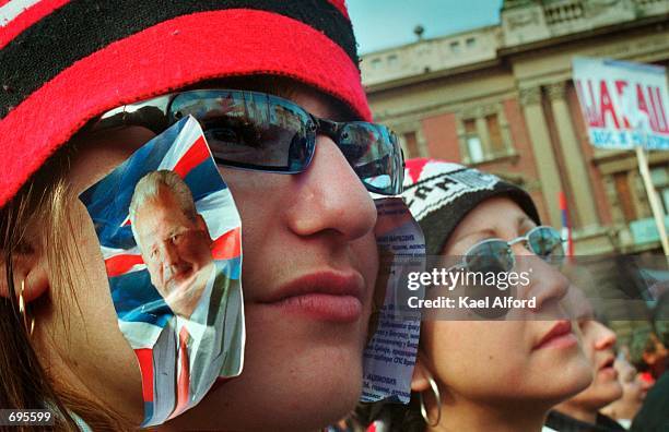 Young woman with pictures of Slobodan Milosevic stuck to her cheeks listens during a rally February 9, 2002 in downtown Belgrade. The crowd gathered...