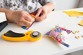 needlework and hand quilting - tailor hands sew multicolored patchwork fabric with the use of needles, cushions for pins, buttons and rotary fabric cutters on white background