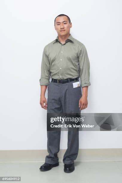 worker wearing button up shirt and slacks standing in front of white wall - grijze broek stockfoto's en -beelden