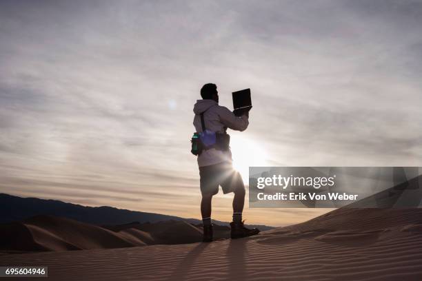 hiker in desert holds laptop high looking for wireless connection - laptop desert stock pictures, royalty-free photos & images