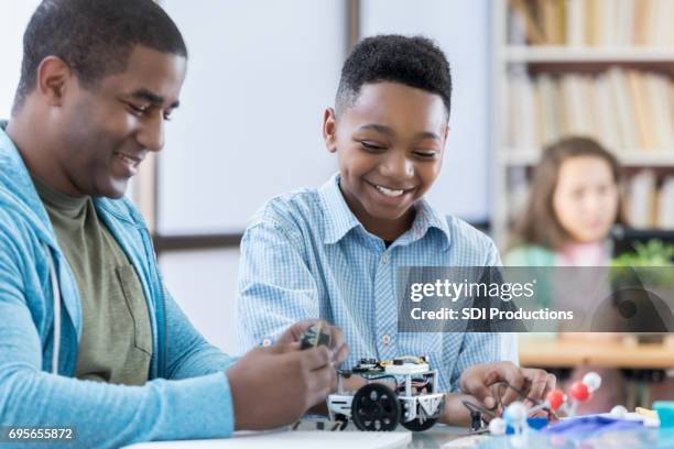 mentor und männliche schüler arbeiten gemeinsam an einem roboter - father and children volunteering stock-fotos und bilder