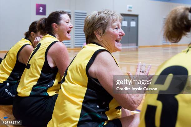 Senior female basketball players sit on bench celebrating beside court