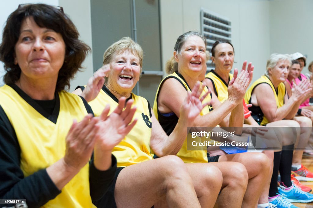 Senior female team players sitting and clapping on indoor court