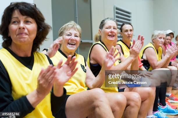 Senior female team players sitting and clapping on indoor court