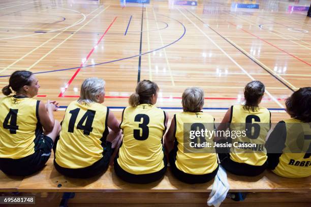 senior female basketball players sit on bench beside court watching the match - woman yellow basketball stock pictures, royalty-free photos & images