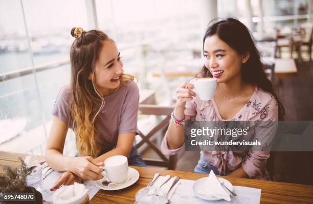 jonge vrouwen drinken koffie en chatten in café - eurasia stockfoto's en -beelden