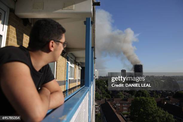 Resident of a nearby council estate watches smoke billowing from Grenfell Tower on June 14, 2017 in west London. - The massive fire ripped through...