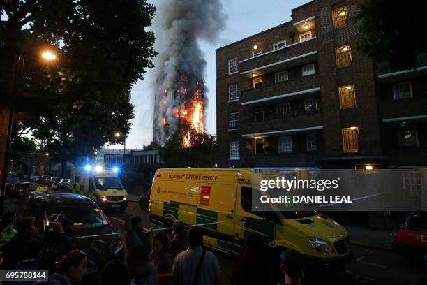 Security cordon holds people backs as Grenfell Tower is engulfed by fire on June 14, 2017 in west London. - The massive fire ripped through the...