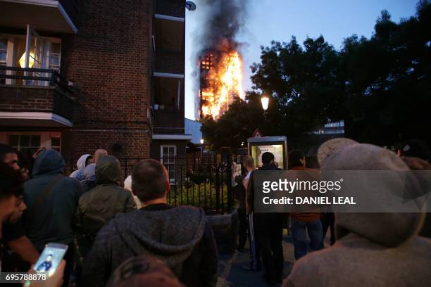Local residents watch as Grenfell Tower is engulfed by fire on June 14, 2017 in west London. The massive fire ripped through the 27-storey apartment...