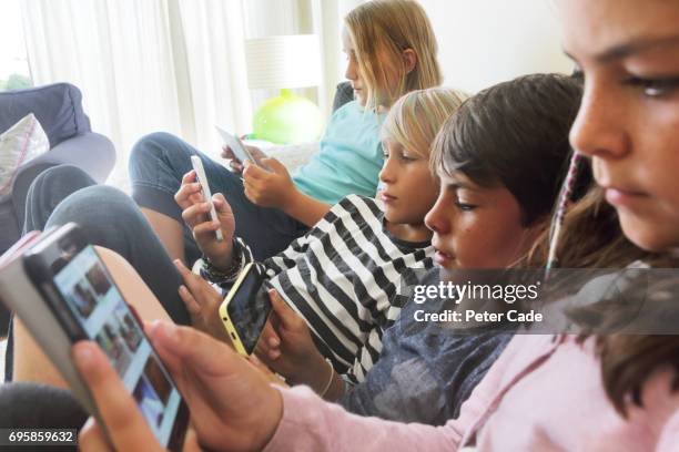 four children sat on sofa looking at phones and tablets - phone addiction stock pictures, royalty-free photos & images