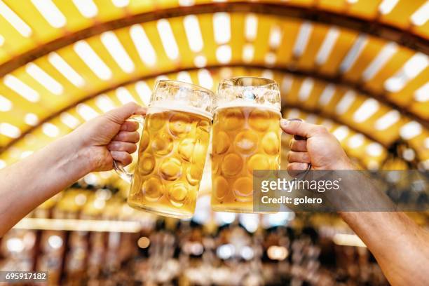 hombre manos tintineantes vasos de cerveza en el oktoberfest en munich - oktoberfest fotografías e imágenes de stock