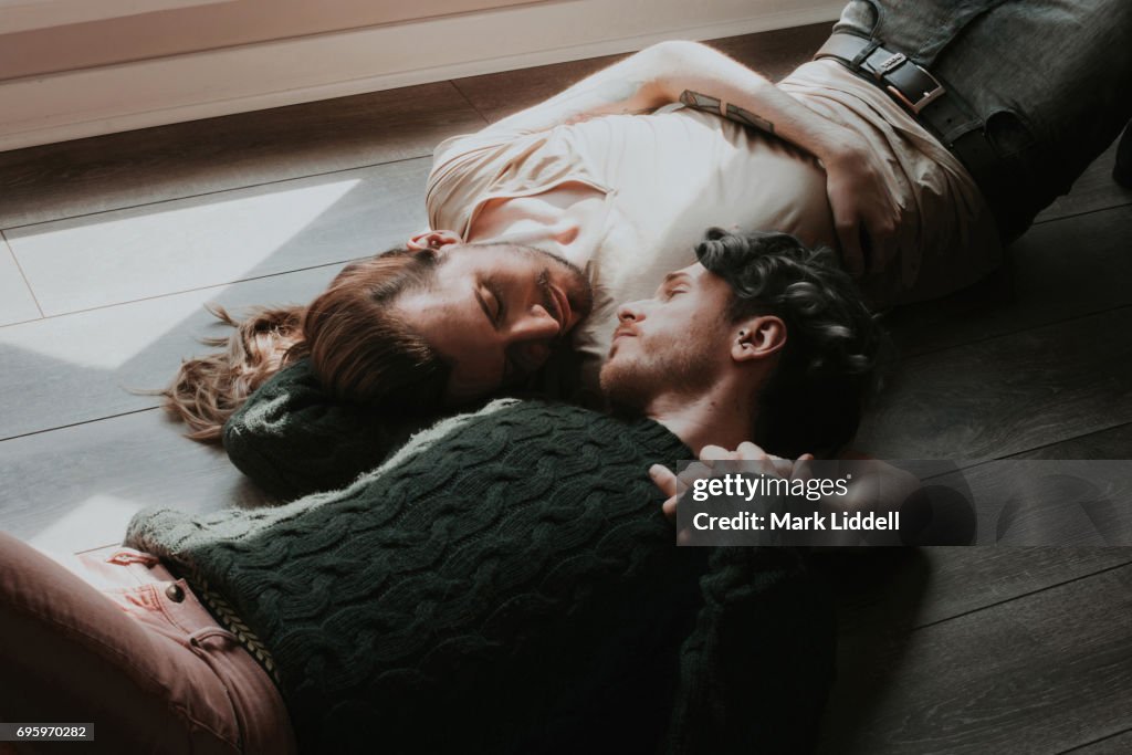 Gay couple lying on floor holding one another.
