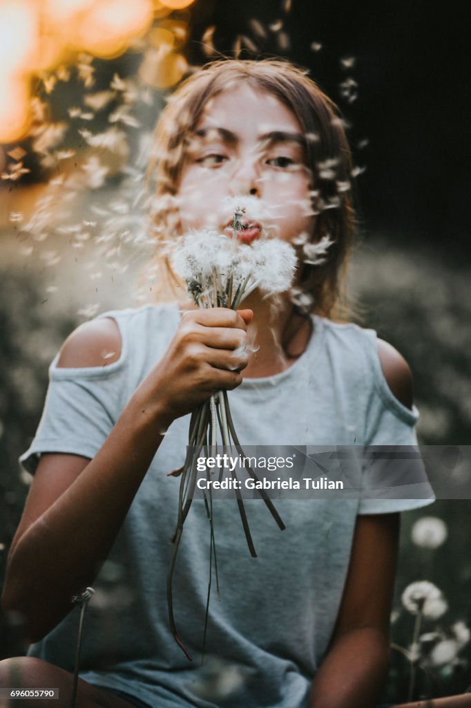 Young girl blowing a dandelion at sunset