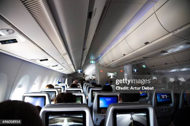 inside of a long distance new airplane with passengers sitting and resting during a long flight with picture taken from the back of the airplane. - inside of plane stock pictures, royalty-free photos & images