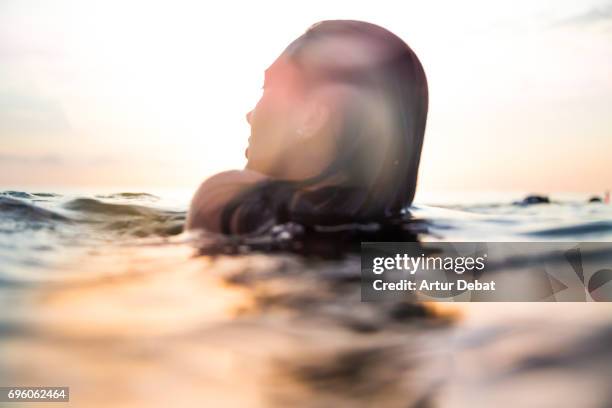 traveler woman floating on water resting during sunset moment after long day during travel vacations in the paradise islands of indonesia with stunning colors in the sky and reflections on water. - moment of silence stock-fotos und bilder