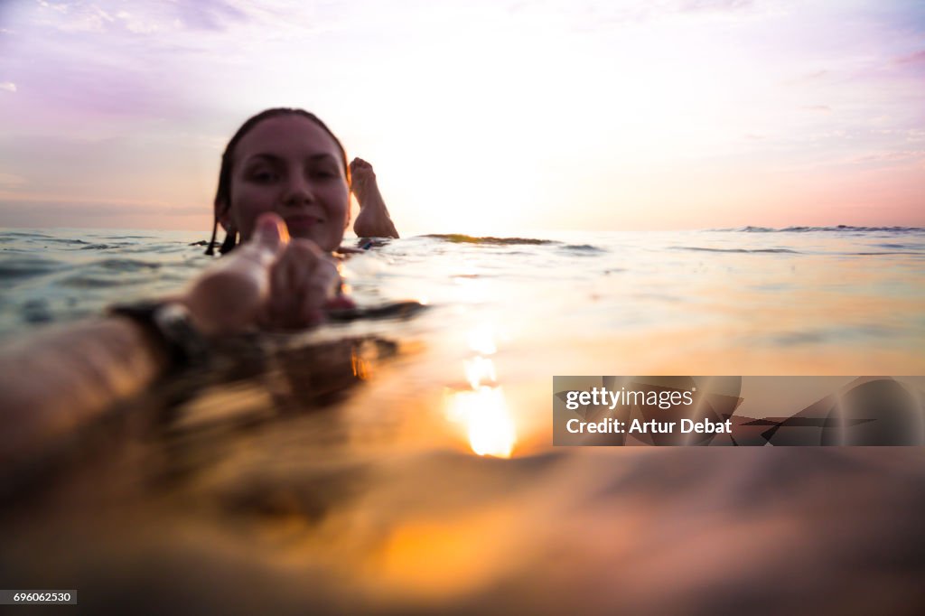 Traveler woman floating on water resting during sunset moment after long day during travel vacations in the paradise islands of Indonesia with stunning colors in the sky and reflections on water holding hand to couple.