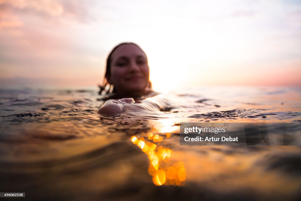 Traveler woman floating on water resting during sunset moment after long day during travel vacations in the paradise islands of Indonesia with stunning colors in the sky and reflections on water holding hand to couple.