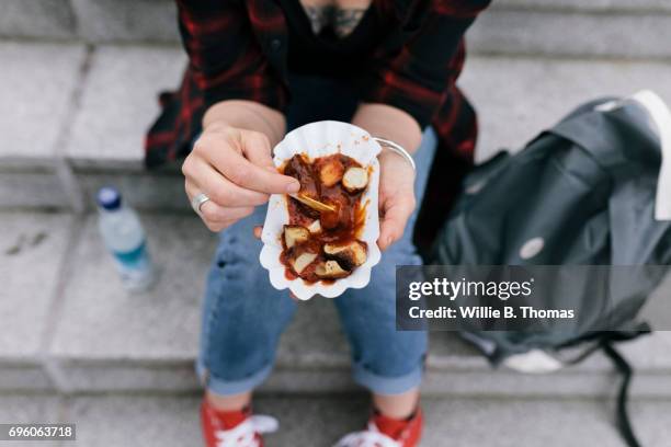woman sitting down on steps eating a currywurst - berlin tourist stock pictures, royalty-free photos & images