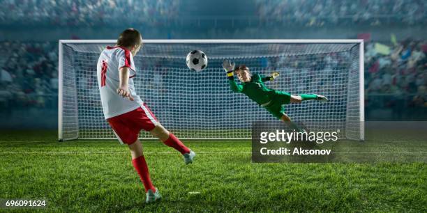 jugador de fútbol niños marcar un gol. el portero intenta golpear la bola - goalie fotografías e imágenes de stock
