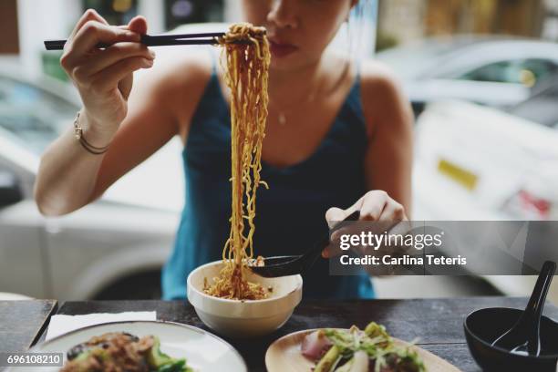 chinese woman eating long noodles on the side of the road - singapore food stock pictures, royalty-free photos & images