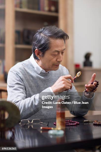 senior man admiring antiques - man sitting at a desk craft stockfoto's en -beelden