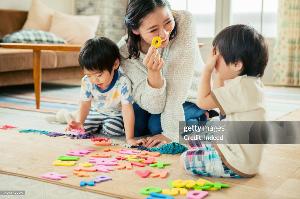 Mother and two boys playing with alphabet puzzles on floor