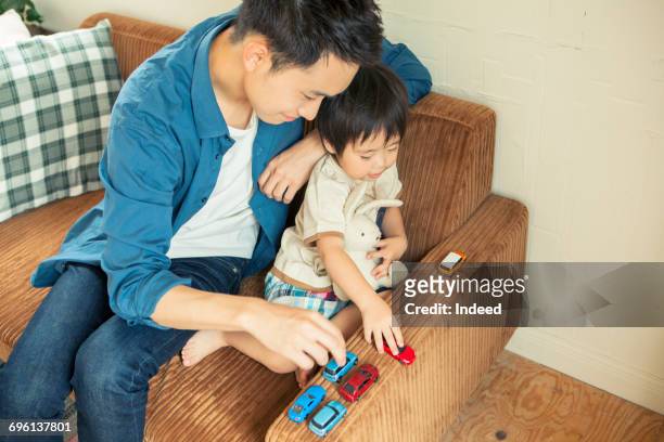 father and boy playing car toys on sofa - auto sofa stock-fotos und bilder