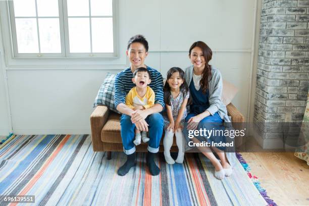 parents and two children smiling on couch - family of four in front of house stock-fotos und bilder