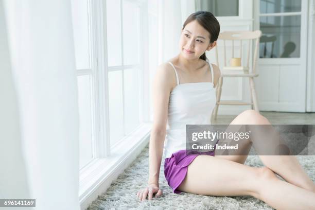 young woman sitting on carpet and looking at view - camisola stock-fotos und bilder