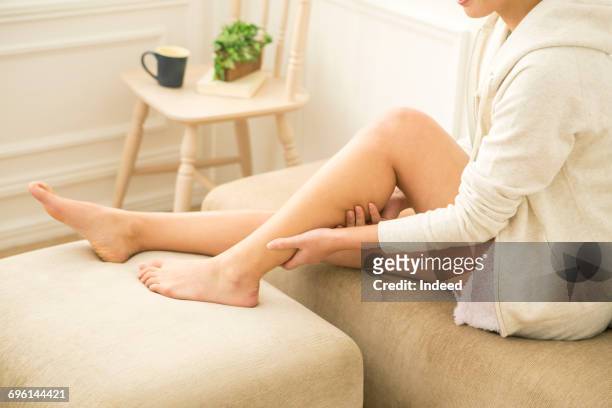 young woman massaging her leg in room - piernas de mujer fotografías e imágenes de stock