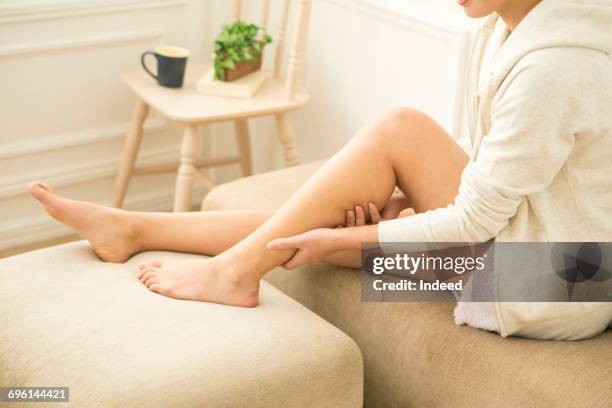 young woman massaging her leg in room - beautiful asian legs - fotografias e filmes do acervo