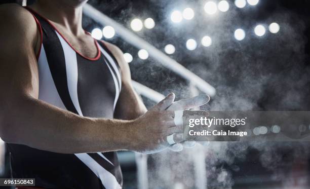 male gymnast rubbing chalk powder on hands below parallel bars - male gymnast stockfoto's en -beelden