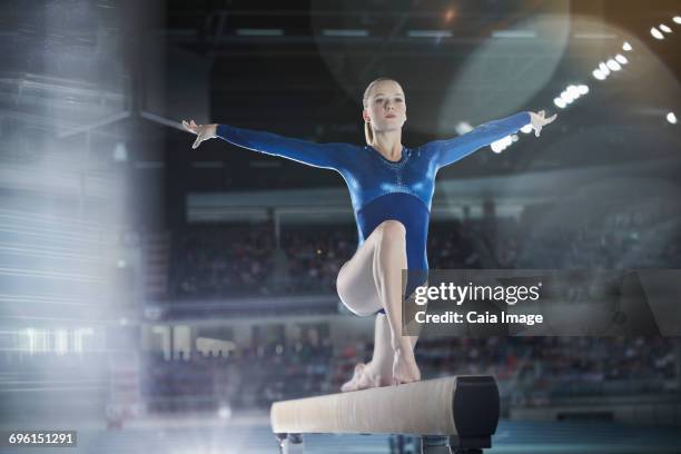 focused female gymnast performing on balance beam in arena - gymnast stock pictures, royalty-free photos & images