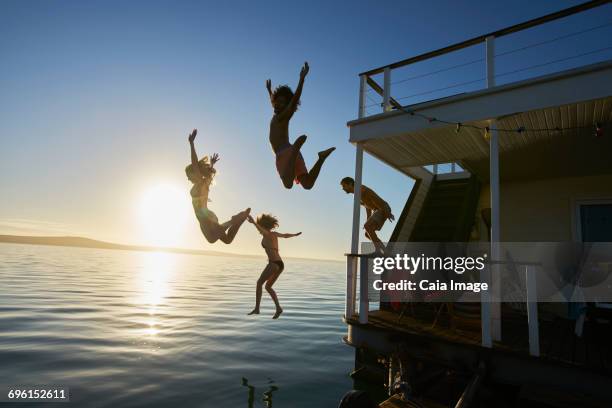 young adult friends jumping off summer houseboat into sunset ocean - houseboat 個照片及圖片檔