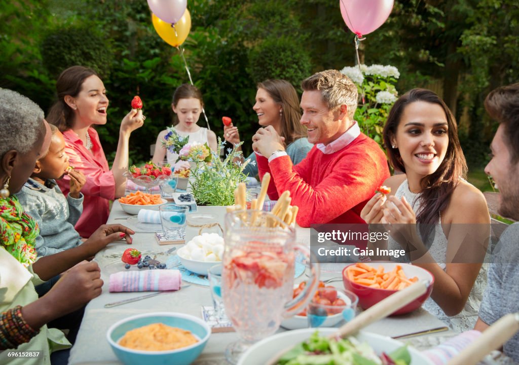 Family and friends enjoying birthday garden party at patio table