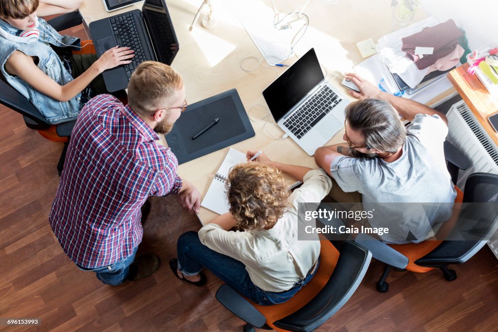 Overhead view design professionals working at laptops in meeting