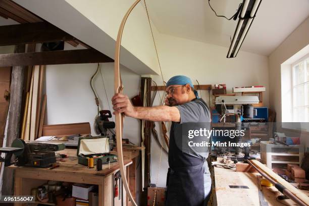 a man testing out a hand made bow by pulling the bow string. - bow and arrow stock pictures, royalty-free photos & images