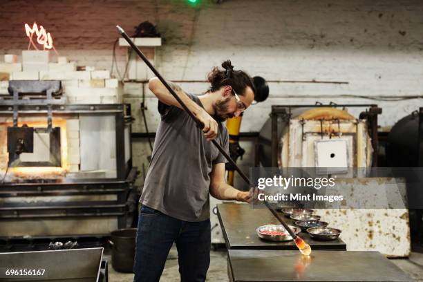 a glassblower holding a piece of molten glass and shaping it on a workbench - glass blowing stock pictures, royalty-free photos & images