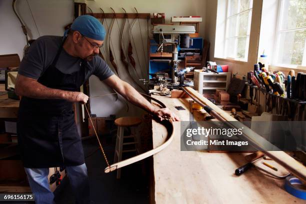 a bowman, a skilled man making a bow, in his workshop. - arco y flecha fotografías e imágenes de stock