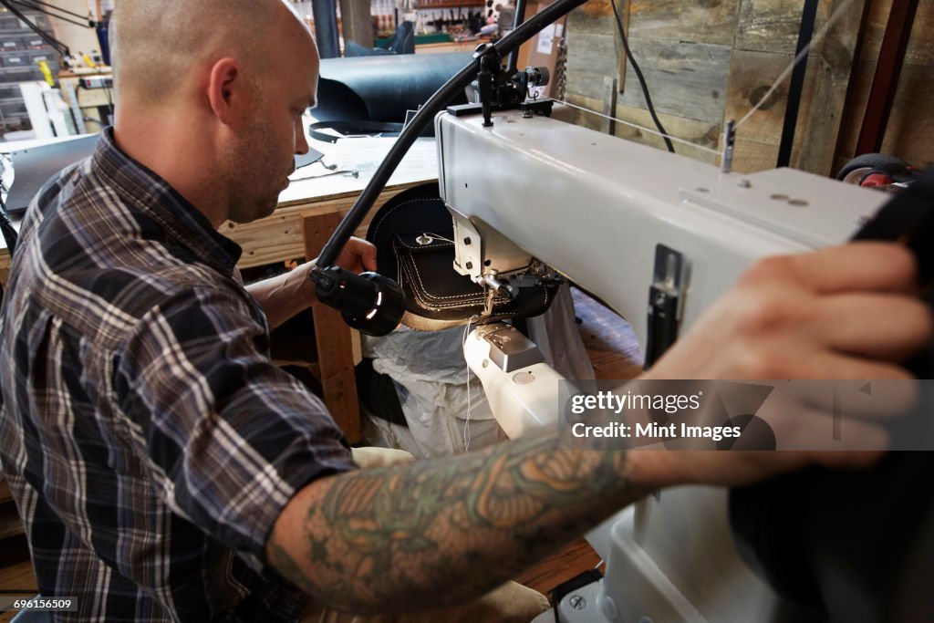 A leather worker, craftsman using an industrial sewing machine on leather material, making a bag.