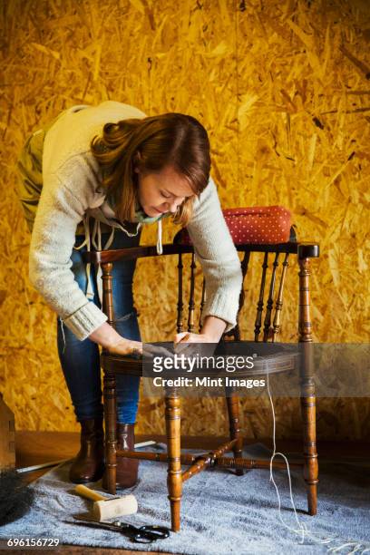 upholstery workshop. a young woman working on a chair seat. - stoffeerder stockfoto's en -beelden