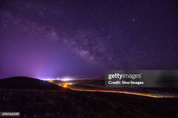 milky way galaxy on purple night sky over vehicle light trails on countryside highway - dali universe stock pictures, royalty-free photos & images
