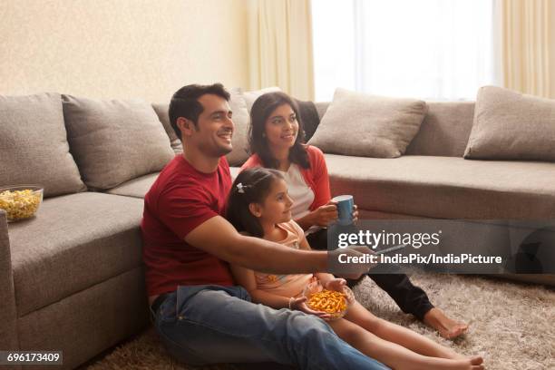 family sitting on carpet watching television - family on couch with mugs stock-fotos und bilder